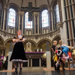 Eine Künstlerin steht mit einer Puppe auf dem Arm vor dem Altar der Herz-Jesu-Kirche in Koblenz. Rechts hinter ihr stehen zwei weitere Künstlerinnen mit weiteren Puppen. 